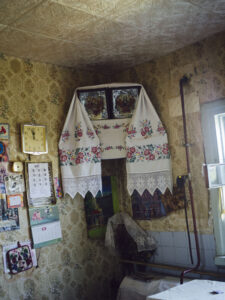 An altar with icons hangs in the corner of a living room. Beside it are wall clocks, calendars and cards.