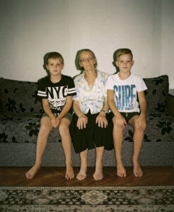 Hanna Šust’ sitting between her two great-grandsons on a sofa.