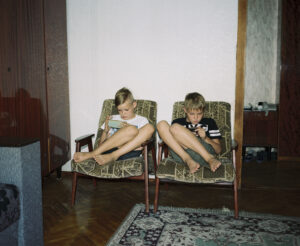 Two children sitting in armchairs next to each other looking at their phones.