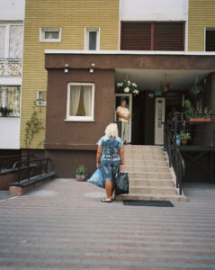 A woman carrying two plastic bags at the entrance to an apartment block.
