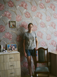 Olha Tarasenko standing in front of a wall with flowery wallpaper, holding onto a chair.
