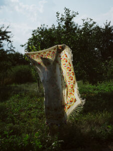 A woman stands in the garden holding an unfolded piece of fabric in front of her.